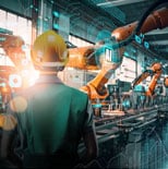 A worker in a hard hat observes robotic arms operating on an automated assembly line in a modern industrial factory.
