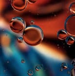 Close-up of several translucent bubbles floating over a blurred, colorful background with shades of blue, orange, and red.